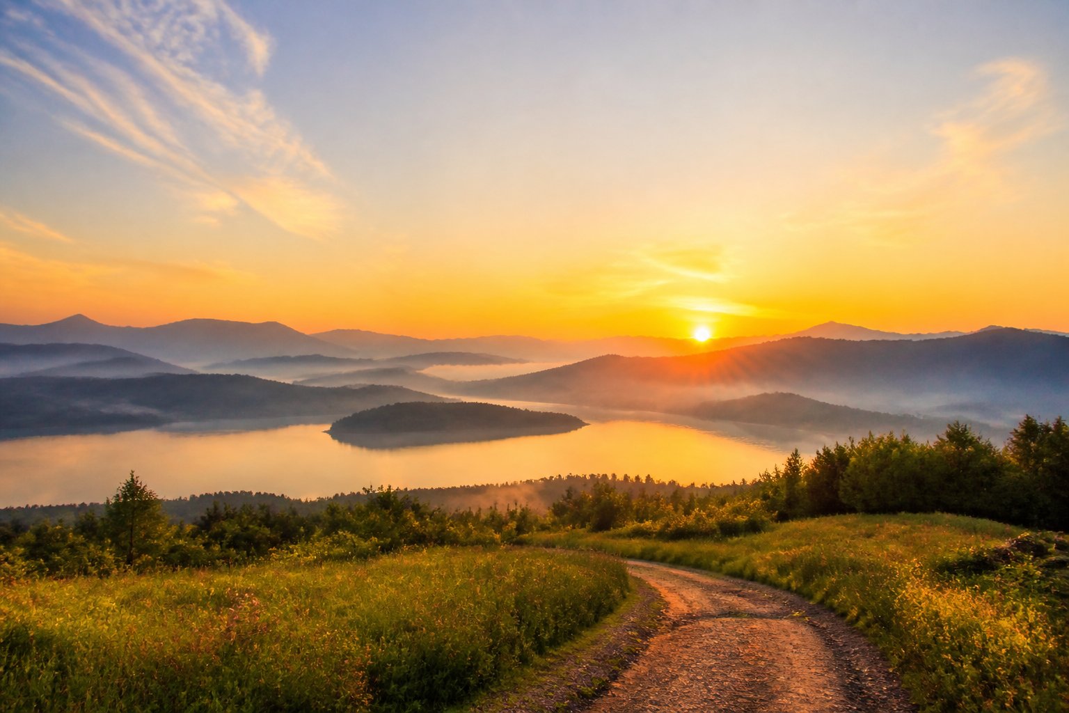 A golden sunrise illuminates misty mountains, a calm lake, and a path leading toward the horizon.